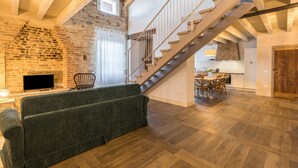 A spacious living area with a wooden staircase, a stone wall, and a modern sofa. - Apartment "Ontano" in Agriturismo Style with Wi-Fi, Garden, and Shared Pool (Desenzano)