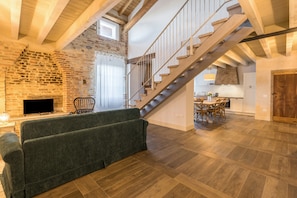 A spacious living area with a wooden staircase, a stone wall, and a modern sofa.