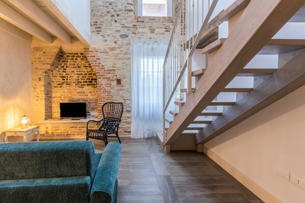 A room with a stone wall, a fireplace, a television, a wooden staircase, and a blue sofa.