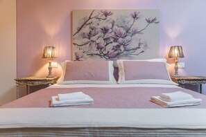 A neatly made bed with two pillows, a bedside table with a lamp, and a wall-mounted painting.