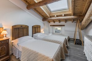 A bedroom with two beds, wooden beams, a skylight, a dresser, and a window with a view.