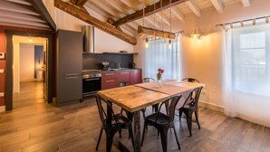 A modern kitchen with a wooden table and chairs, a built-in oven, and a window with curtains. - Modern Loft Apartment "Begonia" with Wi-Fi, Shared Garden & Pool (Desenzano)