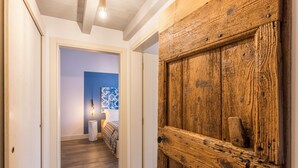A hallway with a wooden door, a bed with a patterned bedspread, and a wall with a blue accent. - Modern Loft Apartment "Begonia" with Wi-Fi, Shared Garden & Pool (Desenzano)