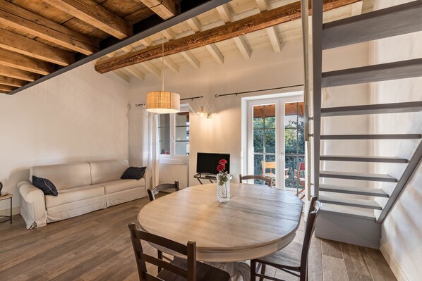 Una habitación con techo de madera, una mesa de comedor redonda con sillas, un sofá, un televisor y una ventana con vistas.