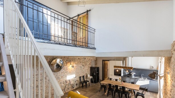 Un'ampia zona giorno con soffitto alto, una scala, un'area pranzo e una cucina.