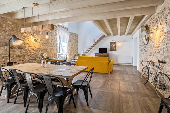 Un coin repas avec une table et des chaises en bois, un canapé jaune, des murs en pierre et un escalier.