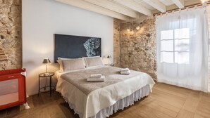 Una camera da letto con parete in pietra, un letto con biancheria bianca, un comodino, una lampada e una sedia rossa.