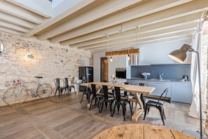 Une cuisine spacieuse avec une table à manger en bois, des chaises noires et un vélo appuyé contre un mur de pierre.