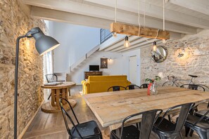 A dining area with a wooden table, black chairs, a yellow sofa, a lamp, and a staircase.