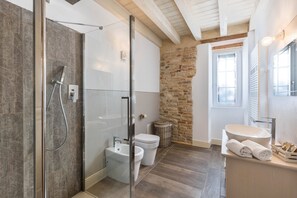 Une salle de bain avec une douche à parois de verre, un lavabo blanc, des toilettes et un mur en pierre.