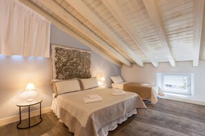 Une chambre avec un plafond en bois, un grand lit recouvert d’une courtepointe blanche, une table de chevet avec une lampe et une fenêtre donnant sur un beau paysage.