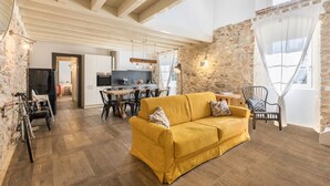 Un soggiorno con un divano giallo, un'area pranzo con tavolo e sedie, una cucina sullo sfondo e un muro in pietra.