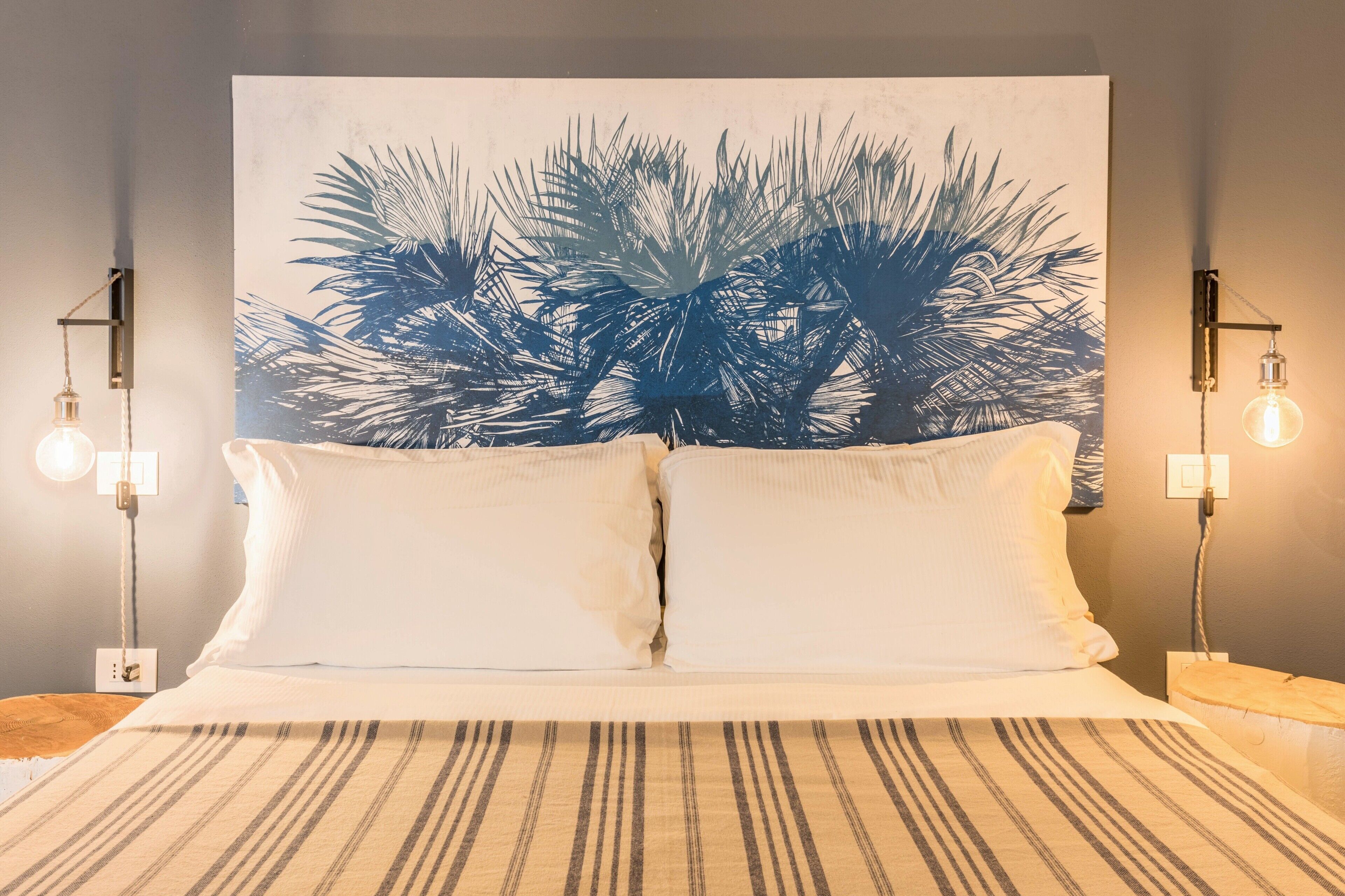A bed with white bedding, a striped rug, and a large wall art of palm leaves.