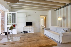 A room with a wooden table, a white sofa, a TV on a white cabinet, and a door leading outside.