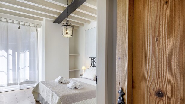 Un dormitorio con cama, mesita de noche, lámpara y ventana con cortinas.
