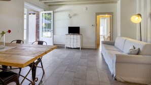 Una sala de estar con una mesa de comedor de madera, un sofá blanco y un televisor sobre un mueble blanco.
