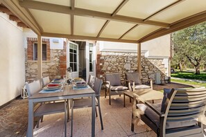 An outdoor patio with a table set for dining, surrounded by chairs, and a covered area with stone walls.