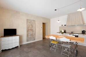 Une cuisine moderne avec une table en bois, des chaises blanches et un téléviseur posé sur un meuble blanc.