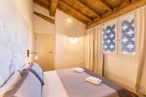 A bedroom with a wooden ceiling, a bed with a patterned bedspread, a wall-mounted light, and a window with curtains.