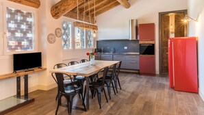 A modern kitchen with wooden beams, a dining table with chairs, a TV, and a red refrigerator. - Large Family Apartment "Rovere" with Wi-Fi, Shared Garden & Pool (Desenzano)