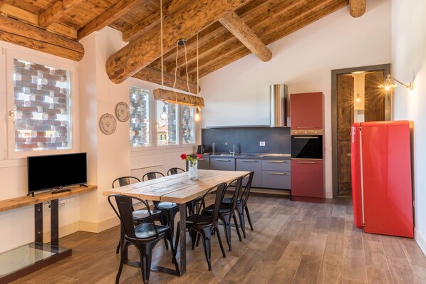A modern kitchen with wooden beams, a dining table with chairs, a TV, and a red refrigerator.