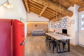 A modern kitchen with a wooden ceiling, a red refrigerator, a dining table with chairs, and a brick wall.