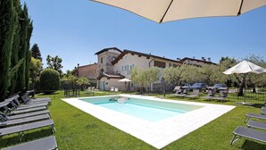 A swimming pool with lounge chairs, a house in the background, and a clear sky. - Large Family Apartment "Rovere" with Wi-Fi, Shared Garden & Pool (Desenzano)