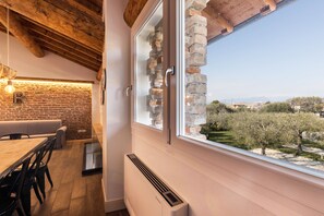 A room with a brick wall, a wooden ceiling, a dining table, and a window with a view of trees and buildings. - Large Family Apartment "Rovere" with Wi-Fi, Shared Garden & Pool (Desenzano)