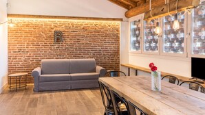 A cozy room with a brick wall, a gray sofa, a wooden dining table, and a vase with red flowers. - Large Family Apartment "Rovere" with Wi-Fi, Shared Garden & Pool (Desenzano)