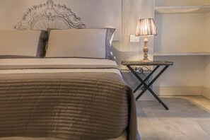 Un lit bien fait, avec une tête de lit, une lampe de chevet et une petite table sur laquelle se trouve une autre lampe.
