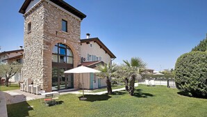 A stone building with a large window, a patio with a table and chairs, and a well-maintained lawn. - Apartment "Ortensia" in Country House Style with Private Garden & Shared Pool (Desenzano)