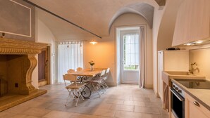 A spacious kitchen with a dining area, a fireplace, and a view through a door. - Apartment "Ortensia" in Country House Style with Private Garden & Shared Pool (Desenzano)