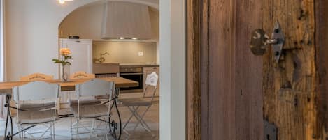 Un comedor con una mesa y sillas de madera, una lámpara colgante y vista hacia una cocina con estufa y horno.