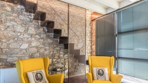 Une pièce avec un mur en pierre, un escalier en métal et deux fauteuils jaunes ornés de coussins.
