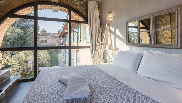 Une chambre avec une grande fenêtre en arc de cercle, un lit avec une literie à motifs, une table de chevet et une lampe.
