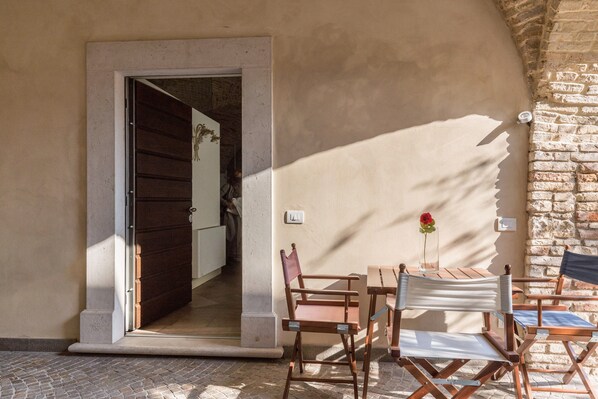 An open doorway leading to a room, a table with chairs, and a brick wall.