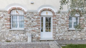 Un edificio de piedra con una puerta blanca, dos ventanas con barrotes de metal y un pequeño balcón.
