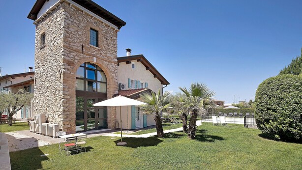 Un edificio de piedra con un gran ventanal, un patio con mesa y sillas, y un césped cuidado.