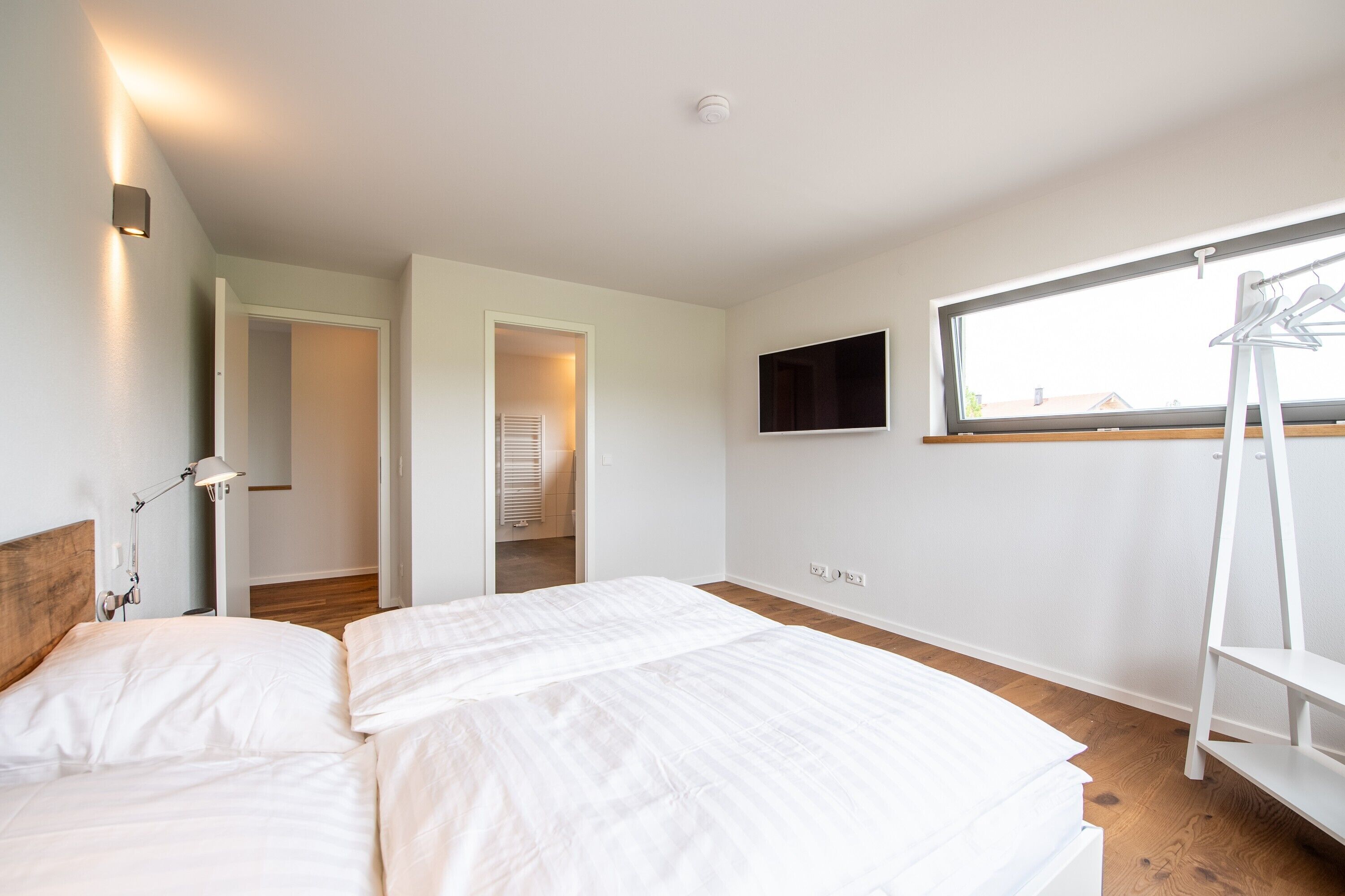 Ein Schlafzimmer mit einem Bett, einem an der Wand montierten Fernseher, einem Fenster und einem Holzboden.