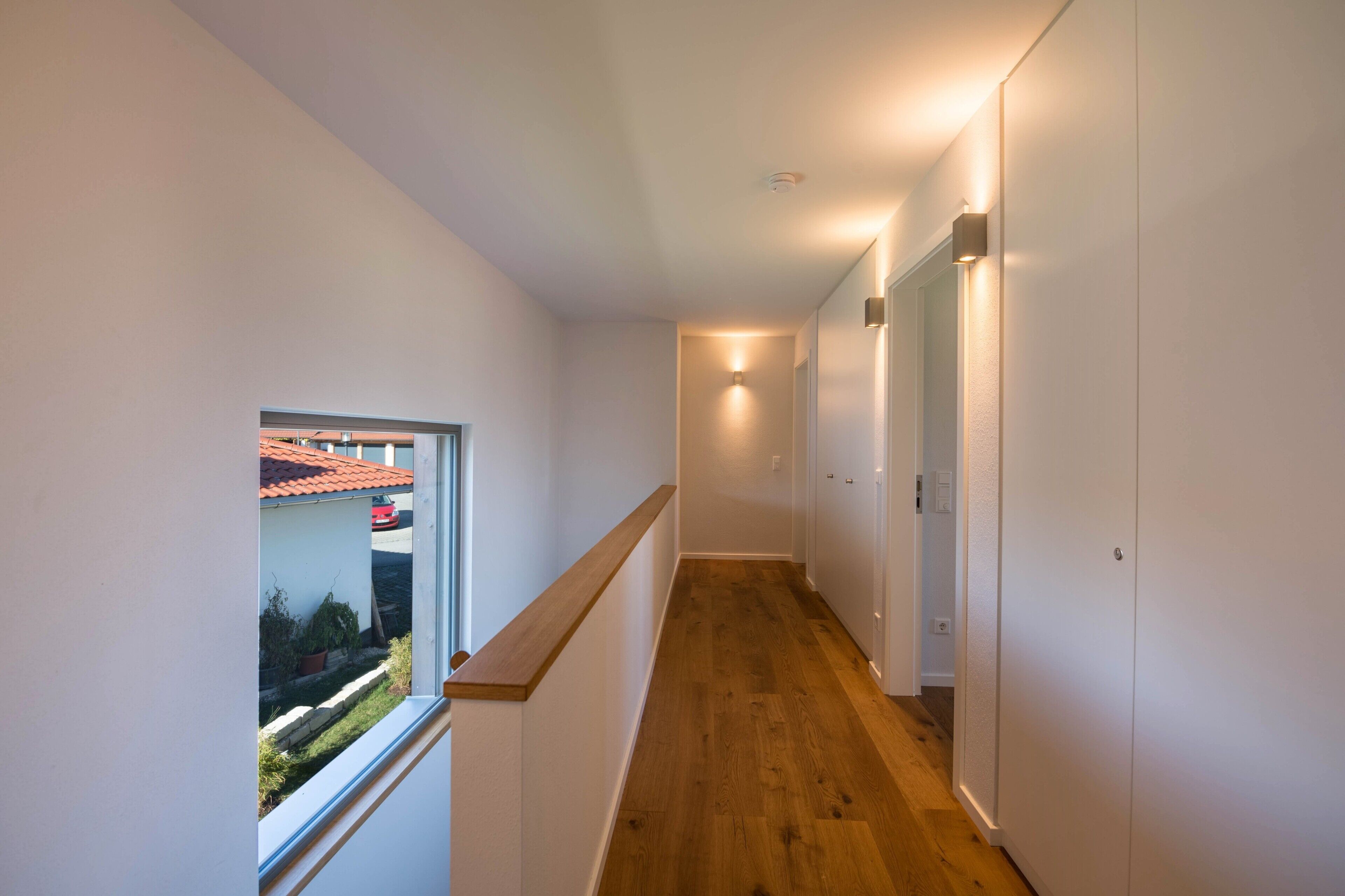 Un corridoio stretto con pavimento in legno, pareti bianche e una finestra che si affaccia su un edificio con tetti rossi.