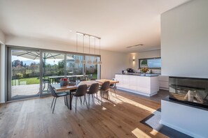 A modern kitchen with a large island, a dining area with chairs, and a sliding glass door leading to a patio. - Luxurious design holiday home with mountain view, fireplace and garden (Breitbrunn am Chiemsee)