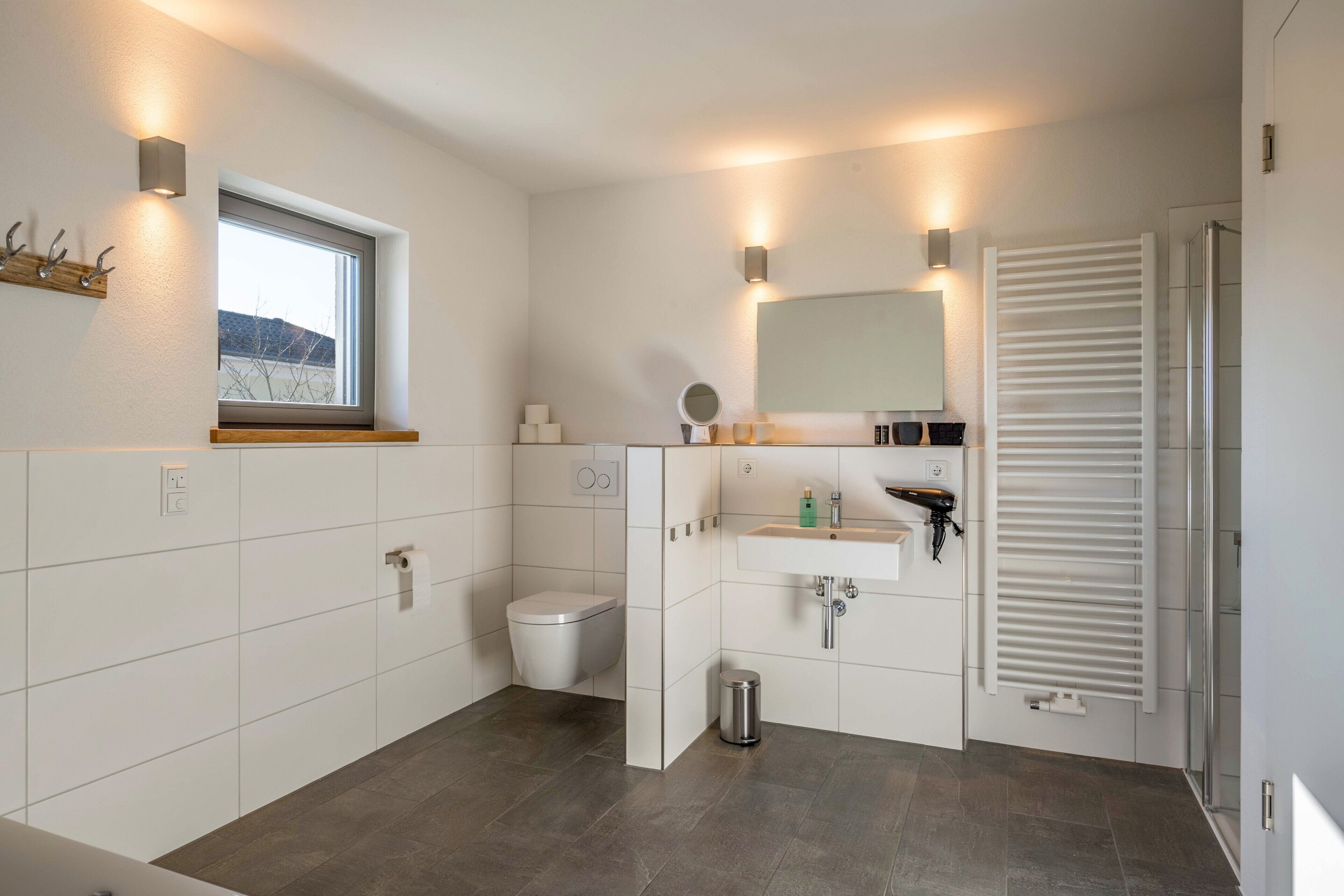 Ein modernes Badezimmer mit Toilette, Waschbecken, Spiegel und Fenster.