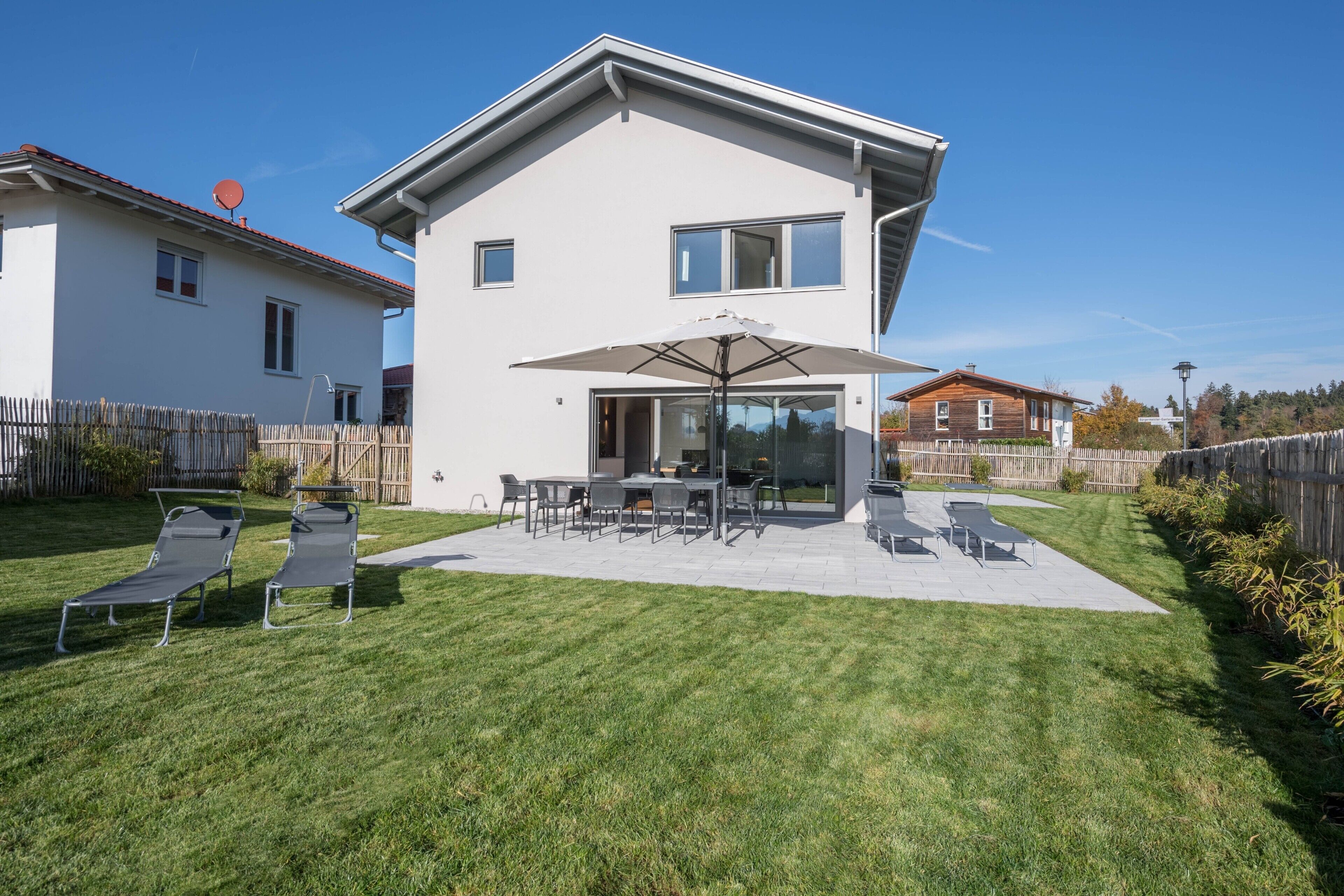 A modern two-story house with a patio, outdoor furniture, and a clear sky.