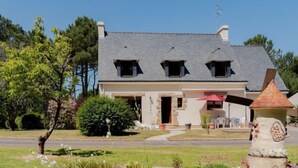 A two-story house with a sloped roof, a front porch, and a small garden area with various plants and a decorative stone structure. - Coët A Tous by Interhome (Carnac)