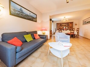 A living room with a grey sofa, colorful cushions, a white coffee table, and a dining area with wooden furniture.