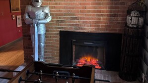 A brick fireplace with a visible fire, a foosball table in front, and a knight statue on the wall. - Harry Potter Castle (Greer)