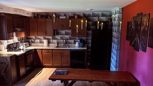 A modern kitchen with wooden cabinets, a black refrigerator, and a wooden dining table. - Harry Potter Castle (Greer)