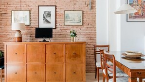 Et værelse med en murstensvæg, et træskab med et fladskærms-TV, et spisebord med stole og billeder i rammer på væggen.