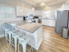 Cozinha moderna com uma ilha grande, banquetas, eletrodomésticos de aço inoxidável e um lustre.
