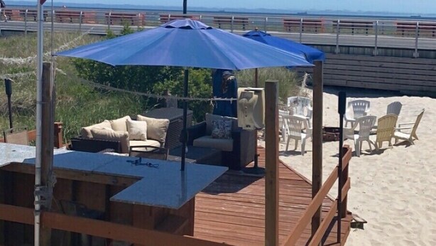 A wooden deck with outdoor seating, a flagpole with multiple flags, and a clear view of the beach. - Cheeseburgers in Paradise (Long Beach)